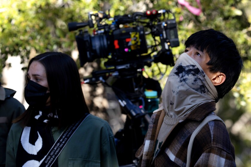 Masked models stand next to a video camera.