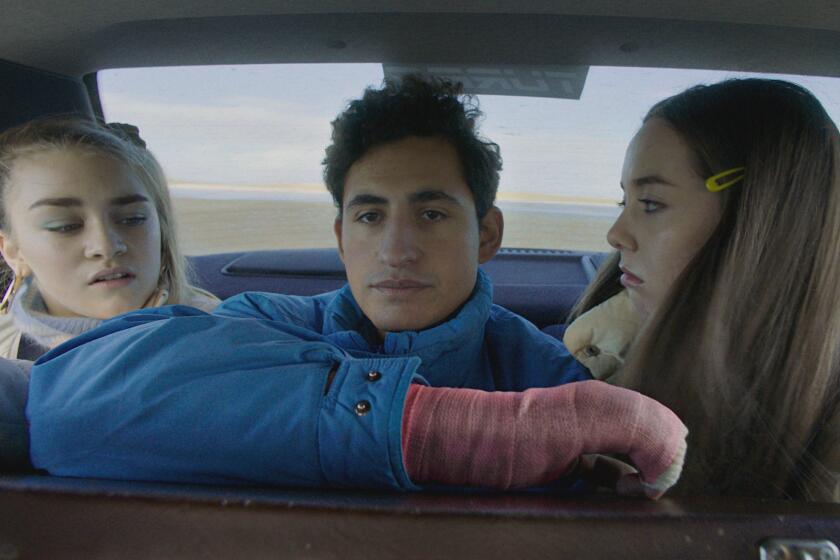 A young man wearing a pink cast sits between two girls in the backseat of a car.