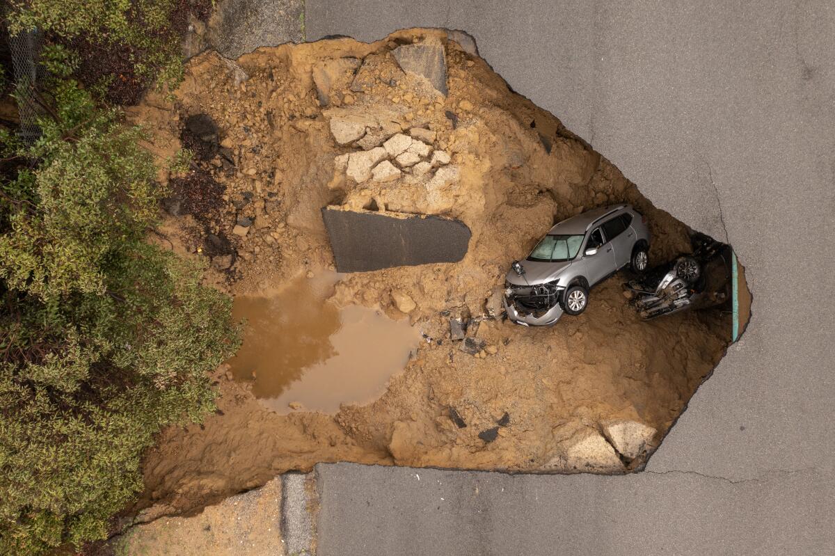 In an aerial view, two vehicles and a pickup truck are seen in a sinkhole 