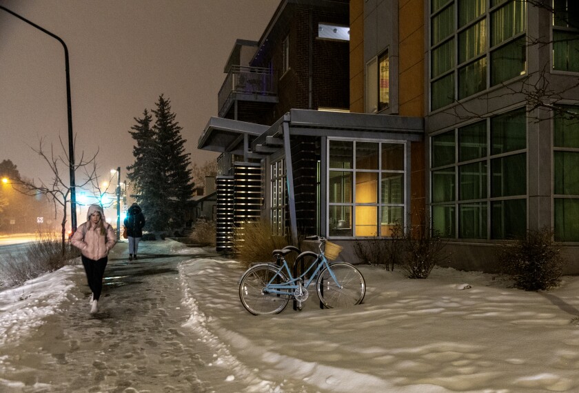 People walk on a snow-covered path in front of a modern apartment building with a bike outside