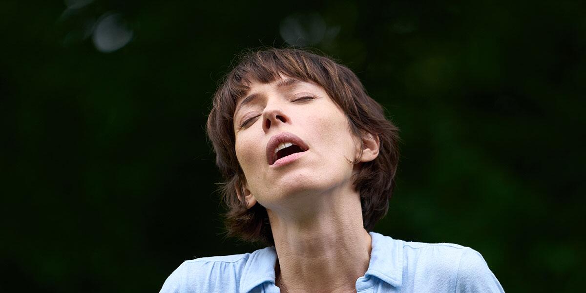 A woman in a blue shirt with her mouth agape and eyes closed.