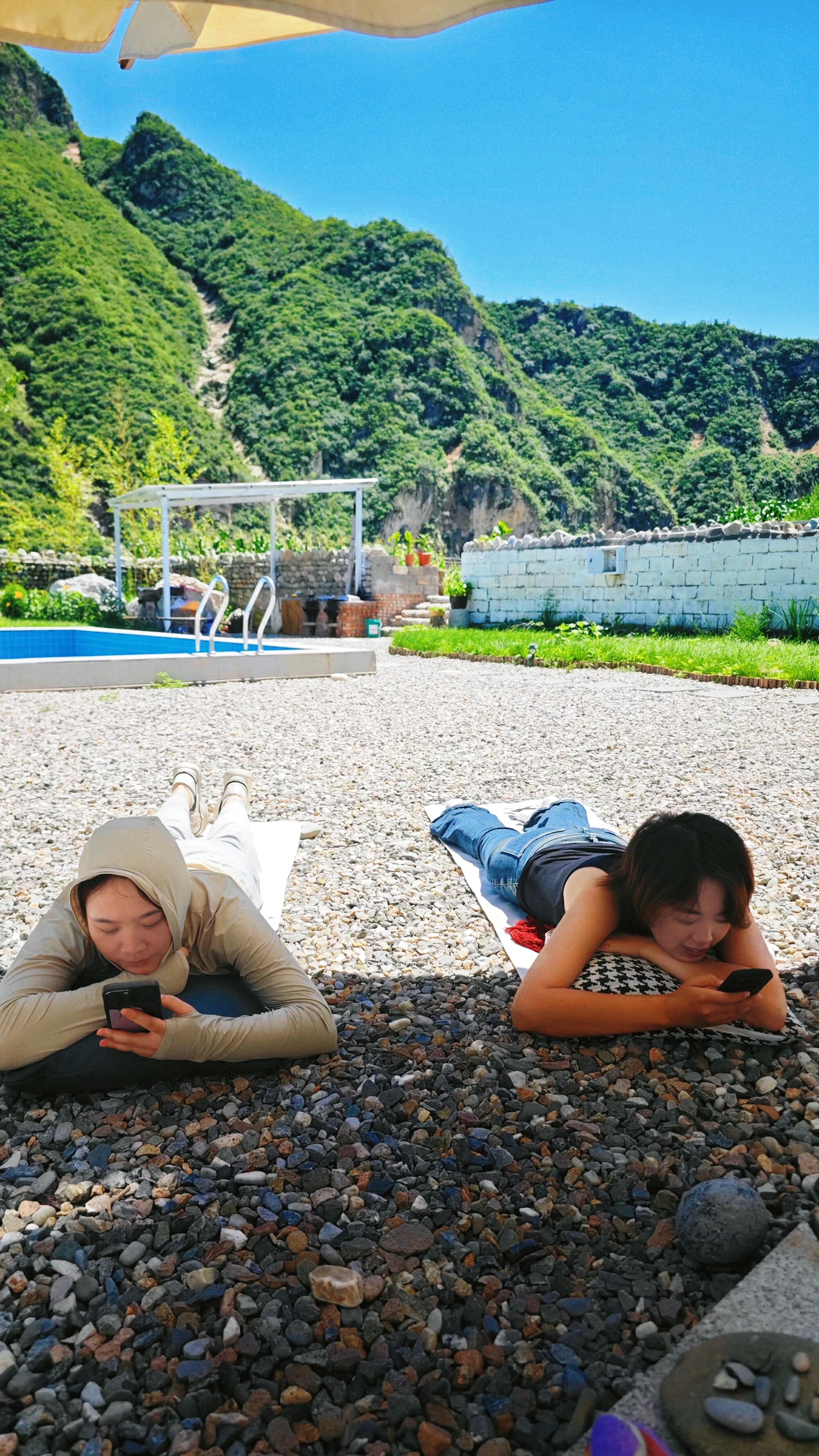 Two young people lie outdoors on their stomachs looking at phones.