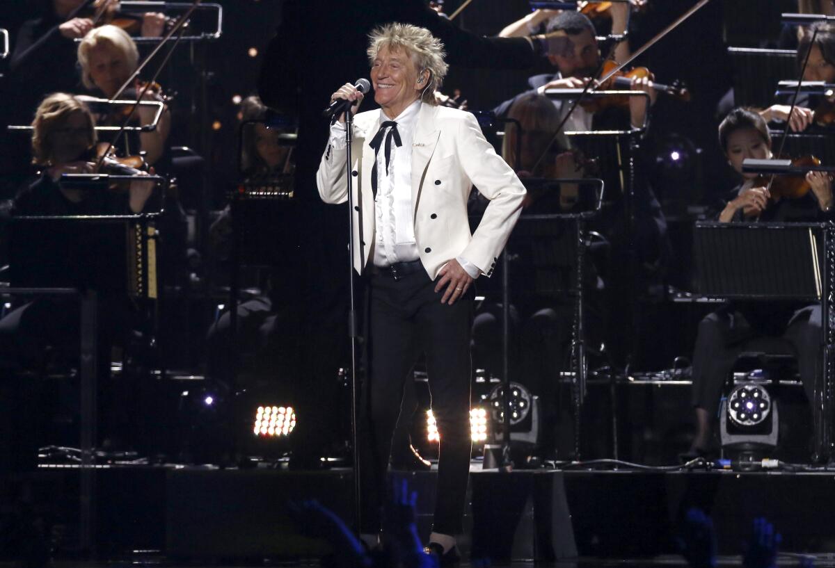 Rod Stewart performs onstage in a white jacket and black pants