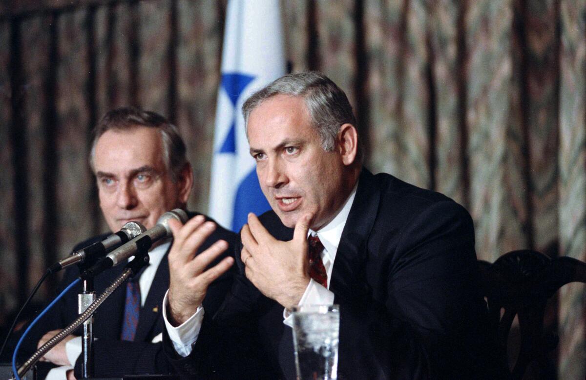 Benjamin Netanyahu, seated, gestures as he speaks into microphones.