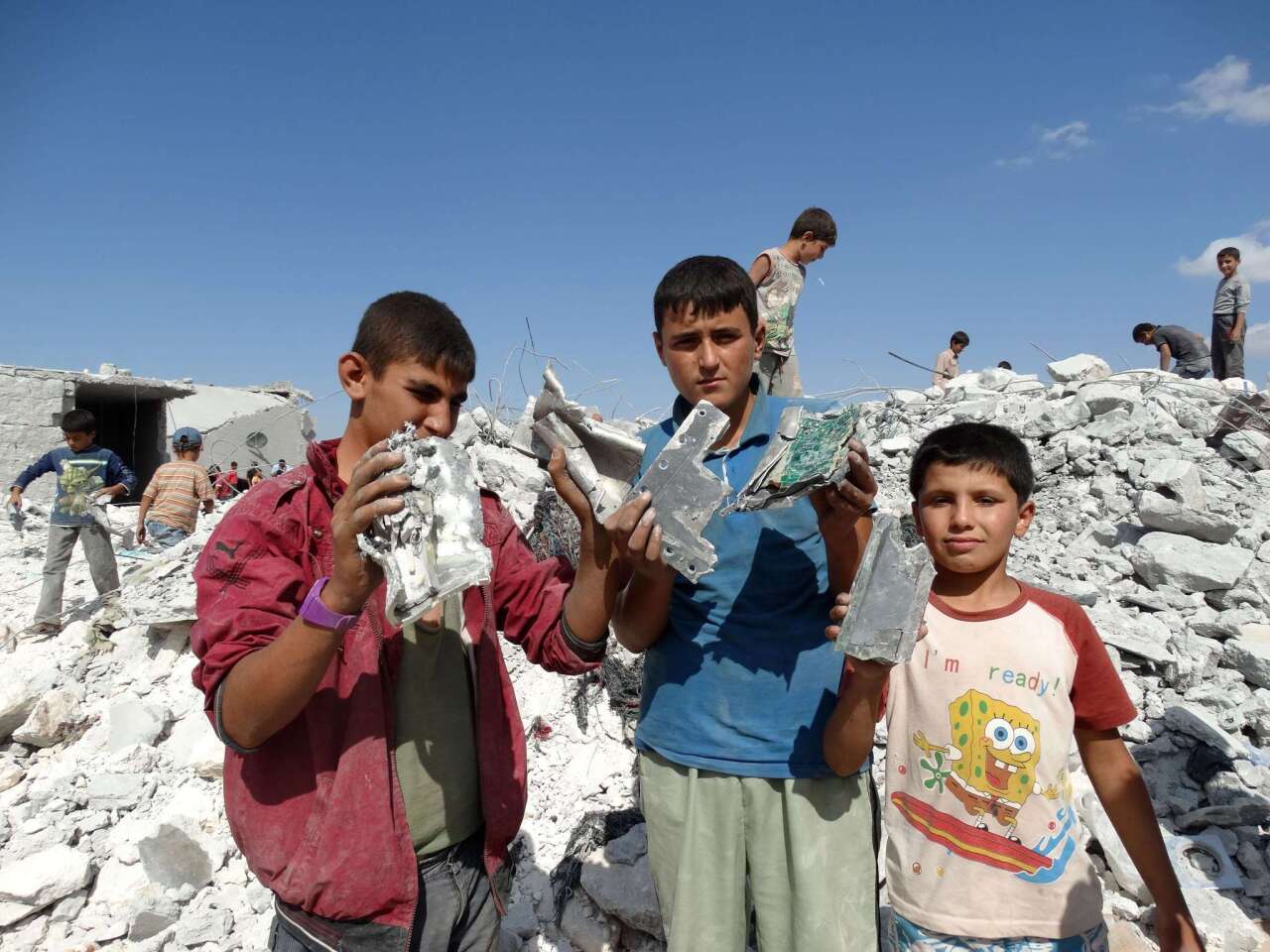 Syrian children hold up debris from a damaged house, reportedly hit by U.S.-led coalition airstrikes, in the village of Kfar Derian in the western Aleppo province.