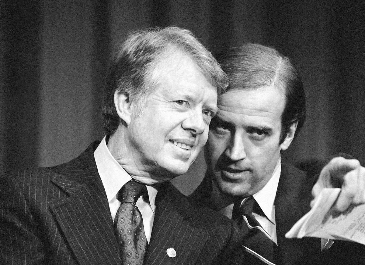 A black-and-white photo of Jimmy Carter listening to Joe Biden, who points off camera