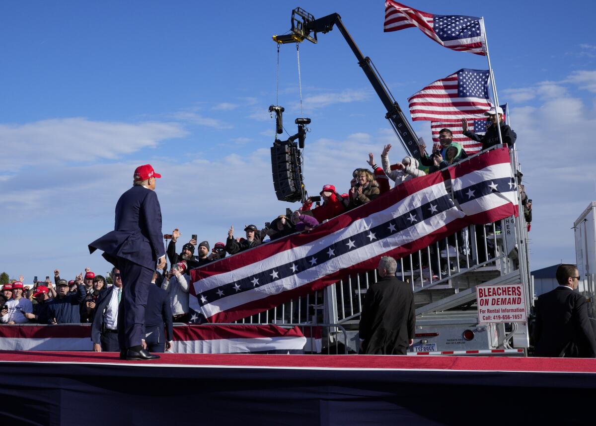 Donald Trump addressing a crowd in bleachers, decorated with flags and bunting,  at an outdoor rally 