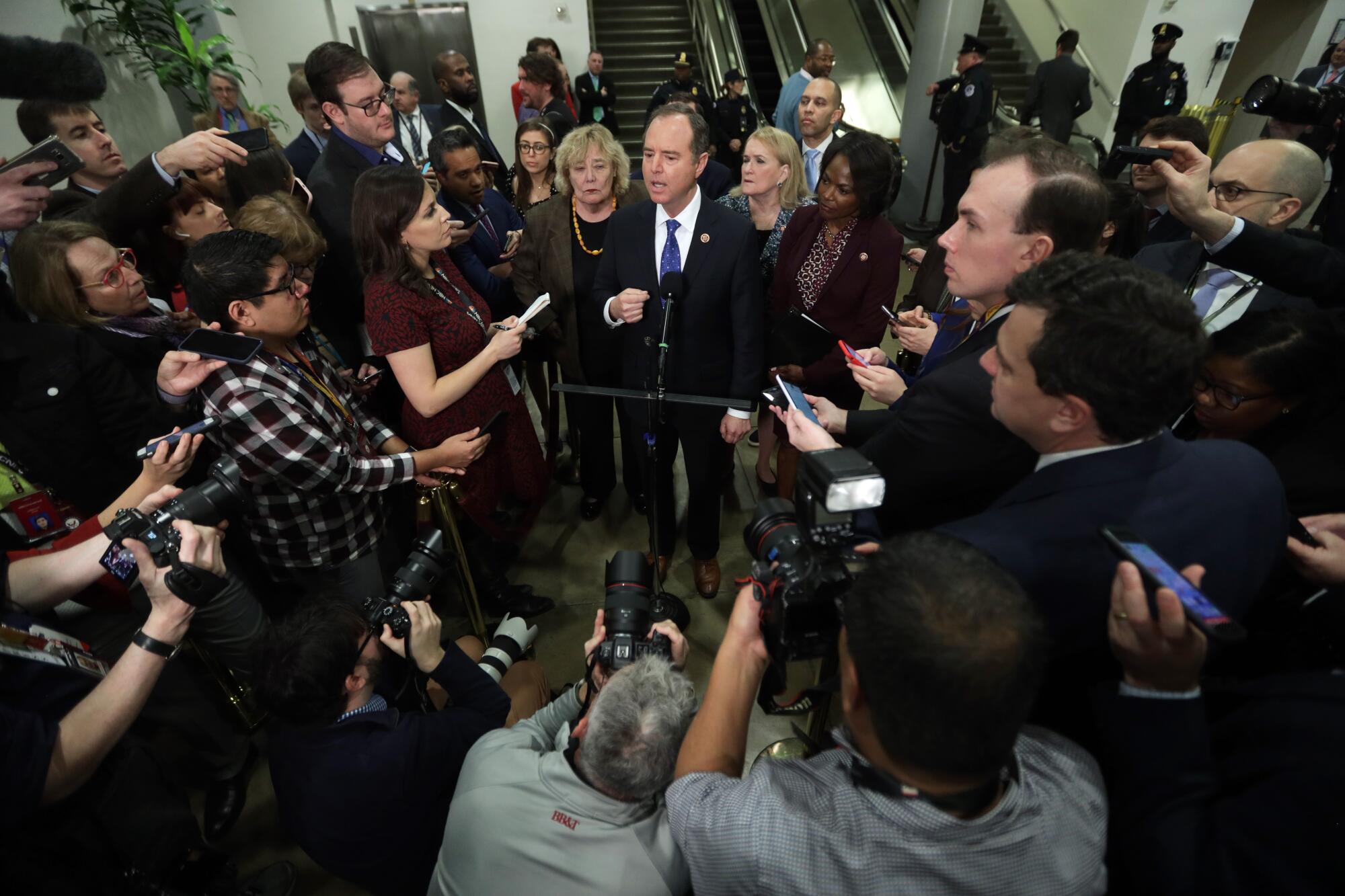 Adam Schiff and fellow House impeachment managers standing, surrounded by members of the news media, as he speaks into a mic