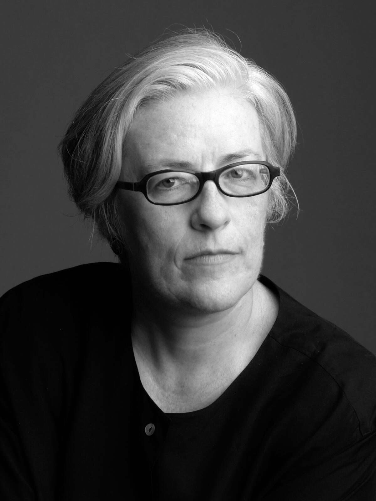A black-and-white headshot of Cynthia Carr, with short hair, glasses and a black shirt.