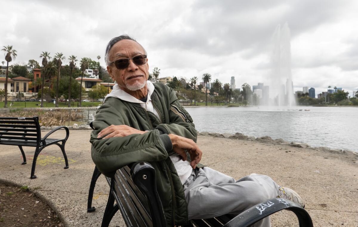 Gil Mangaoang sits on a bench in front of the Echo Park Lake fountain.