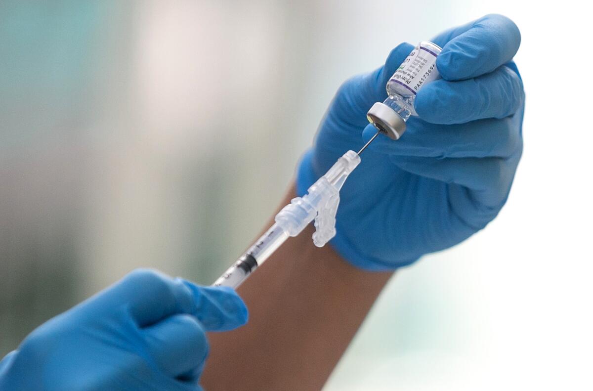 Gloved hands use a syringe to pull liquid out of a small glass vial