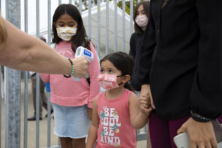 San Diego, CA - August 30: From left, Valentina Zapata, 9, watches as her sister, Paloma, 3, has her temperature checked before heading to her first day of school at the San Diego Cooperative Charter Schools on Monday, Aug. 30, 2021 in San Diego, CA. The school is kindergarten through eighth grade and has a total of 460 students. Students' temperatures will be checked daily before entering the campus. Last year, the school had zero COVID-19 transmissions on campus. (Ana Ramirez / The San Diego Union-Tribune)