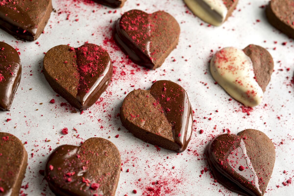 Chocolate shortbread heart cookies are dipped in chocolate, then sprinkled with colorful freeze-dried raspberries.