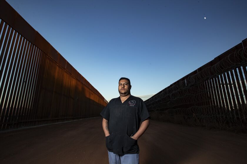 NACO, AZ - NOVEMBER 23: Veterinary assistant Jesus Tarazon stands for a portrait between the new border wall and the old wall Monday, Nov. 23, 2020 in Naco, AZ. Tarazon commutes to his job Bisbee from his home in Naco daily. "Some day soon, I hope life returns to normal," he said. "All of us, Americans, Mexicans, Mexican Americans, have been hurting from this pandemic." (Brian van der Brug / Los Angeles Times)