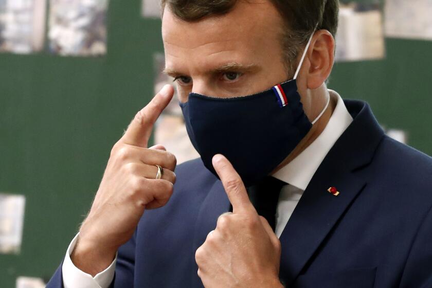 FILE - In this May 5 2020 file photo, French President Emmanuel Macron wears a protective face mask as he speaks with schoolchildren at the Pierre Ronsard elementary school, outside Paris. The French praised the altruism of luxury goods companies such as LVMH, Kering and Chanel for diverting their production facilities to make millions of face masks for the public during the peak of their country's coronavirus outbreak. Now, the companies that helped France avoid a dangerous shortage say they need help unloading a surplus of 20 million washable masks. (Ian Langsdon, Pool via AP, File)