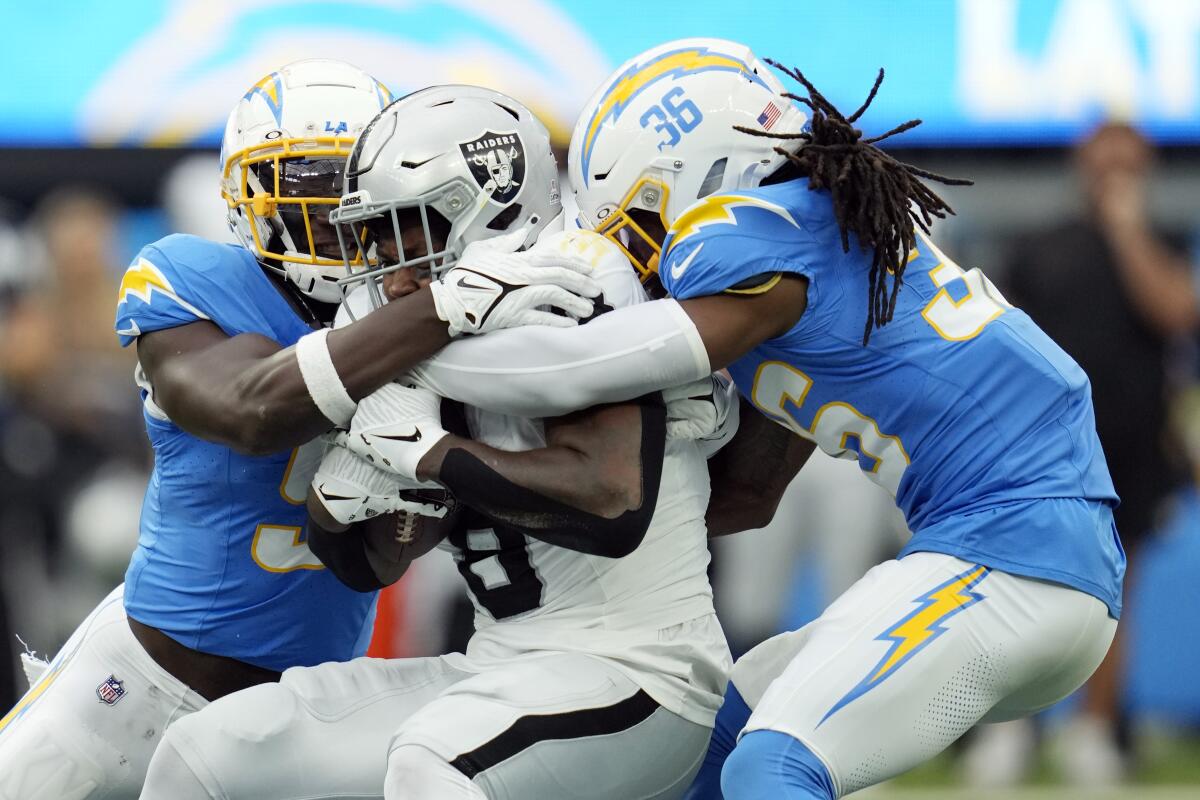 Raiders running back Josh Jacobs is tackled by Chargers' Kenneth Murray Jr. and Ja'Sir Taylor.