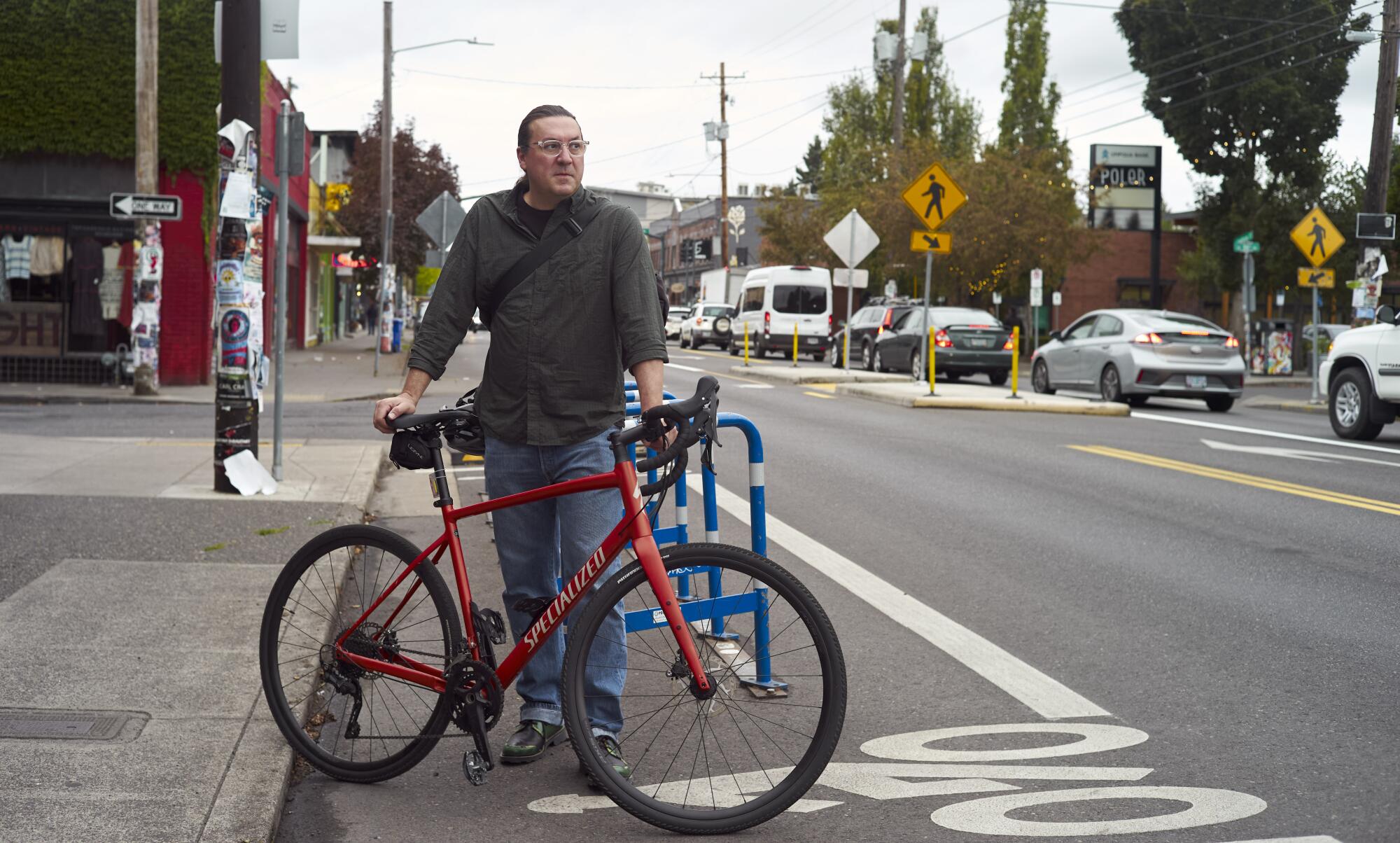 A man stands in a bike lane with his red bike.