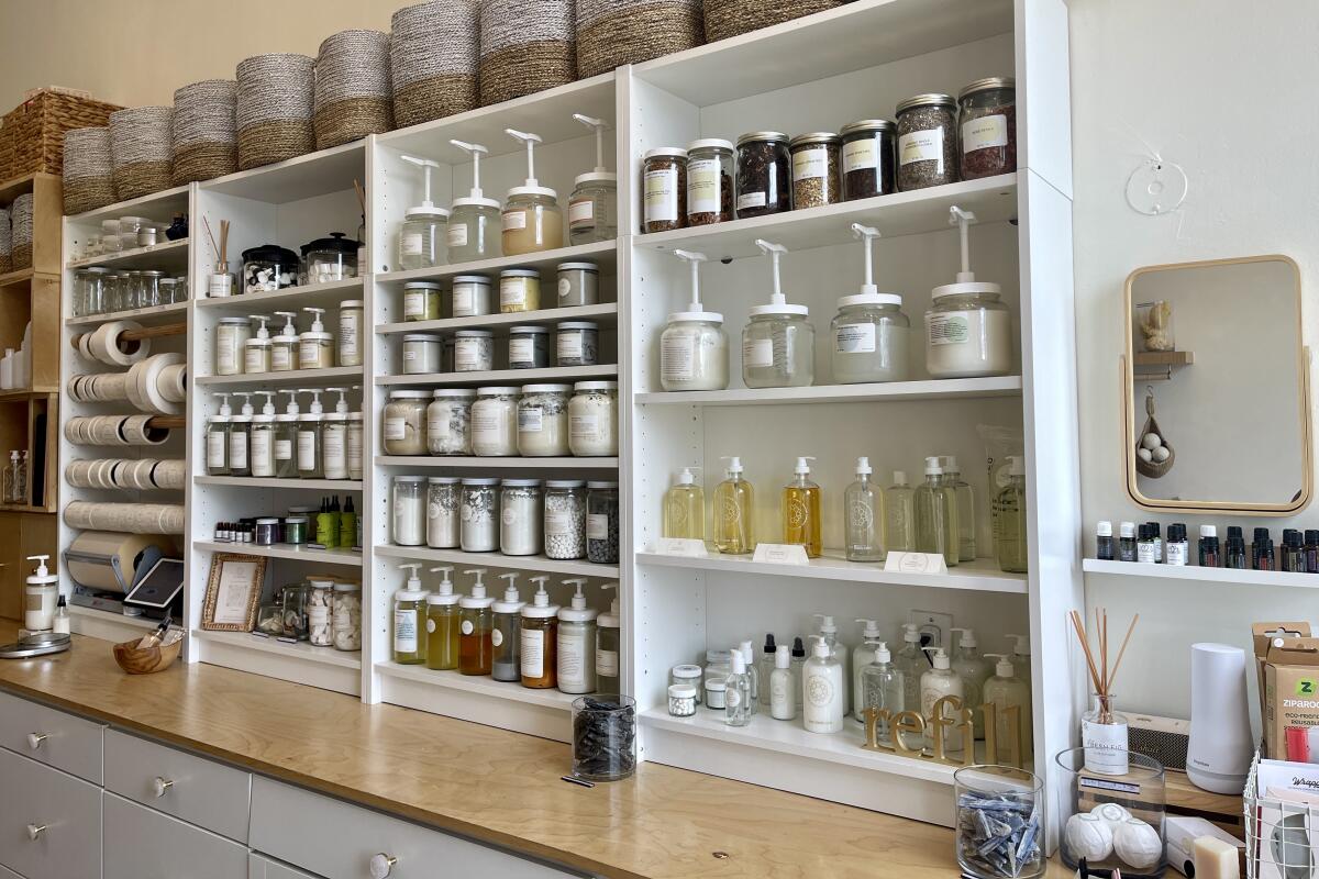A wall of glass jars and pump bottles on white shelves containing cleaning and beauty products.
