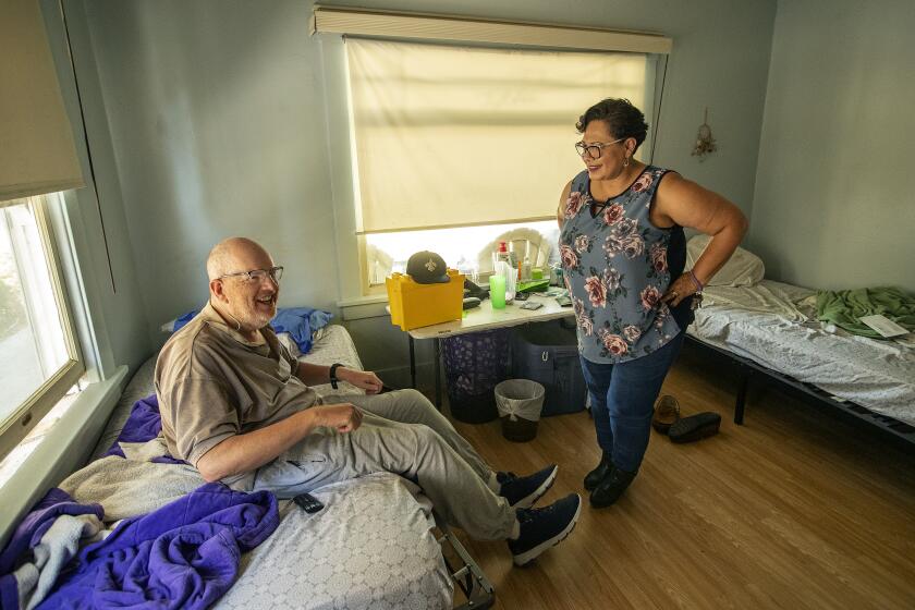 PASADENA, CA-JUNE 30, 2023: Desiree Alvarado, who owns and operates a board and care home in Pasadena, talks with resident Kevin Taylor, 58, inside his room that he shares with another resident. Alvarado bought the property in 2008 and she and her family have run it since. Alvarado says It's incredibly hard to stay open given the low reimbursement rates. (Mel Melcon / Los Angeles Times)