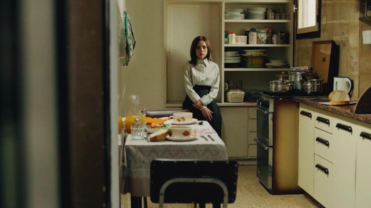 A woman stands alone in a kitchen with her arms crossed in front of her.