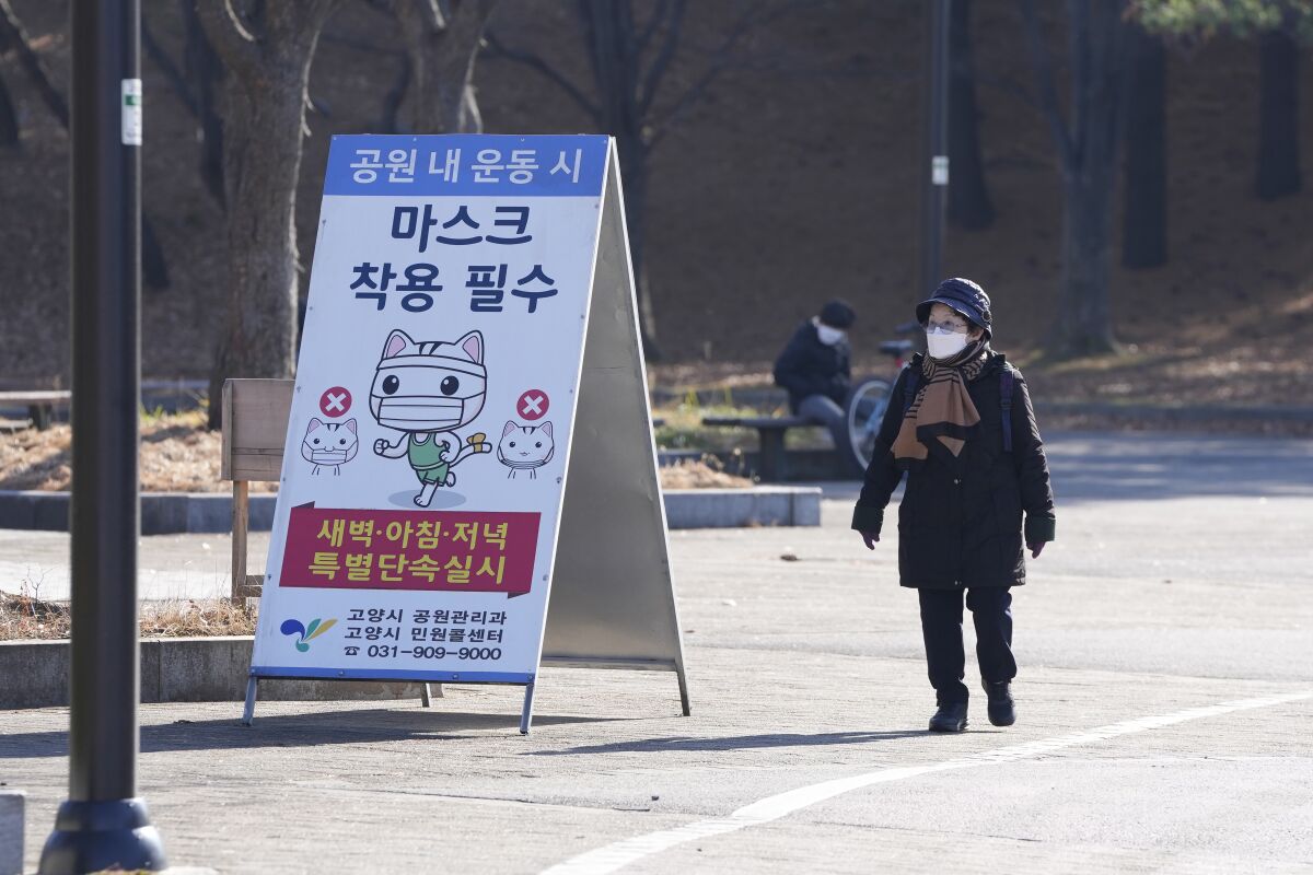 A visitor wearing a face mask as a precaution against the coronavirus, walks near a banner at a park in Goyang, South Korea, Saturday, Dec. 4, 2021. South Korea again broke its daily records for coronavirus infections and deaths and confirmed three more cases of the new omicron variant as officials scramble to tighten social distancing and border controls. The banner reads "Mandatory mask wearing." (AP Photo/Lee Jin-man)