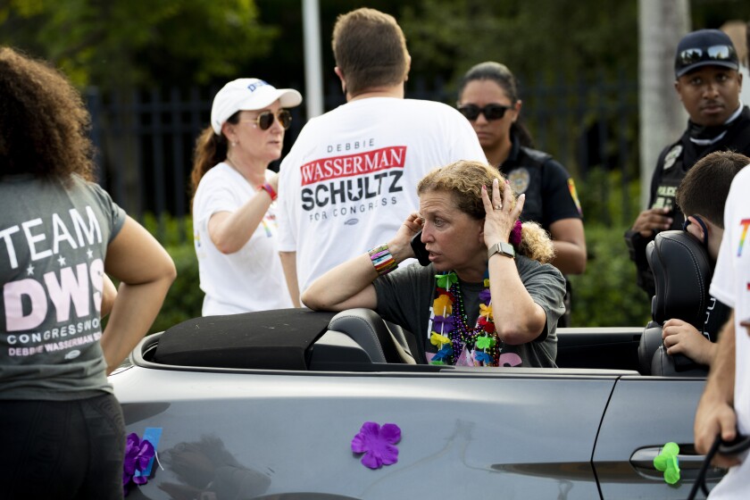 A woman talks on the phone while sitting in a convertible at a parade