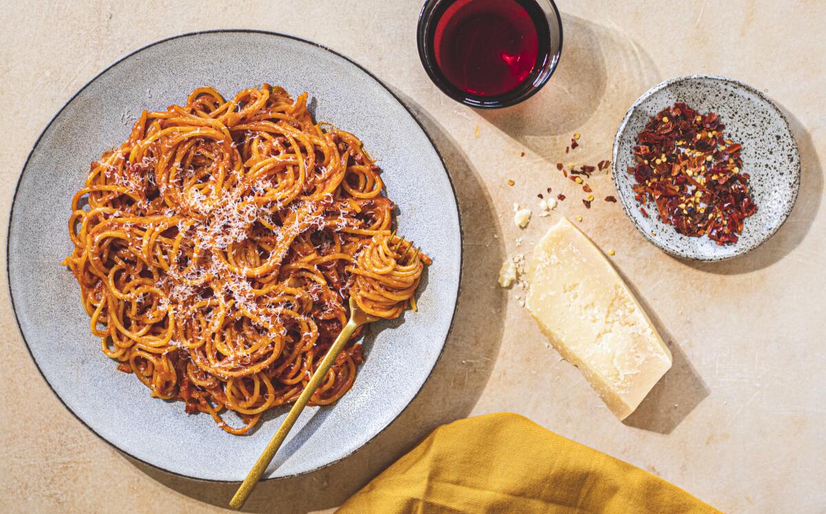 A plate of spaghetti with red pepper flakes and a hunk of white cheese