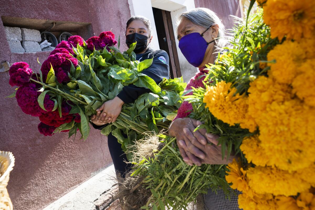 Two women wearing facemasks hold huge bundles of flowers