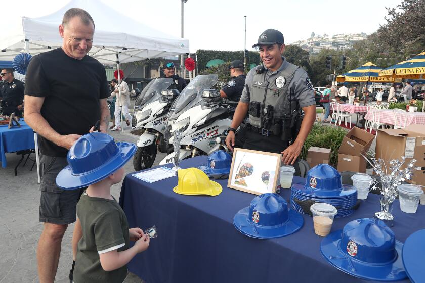 Park Ranger Oscar Perez, right, hands out ranger hats to families during National Night Out activities at Main Beach Park in Laguna Beach on Tuesday.