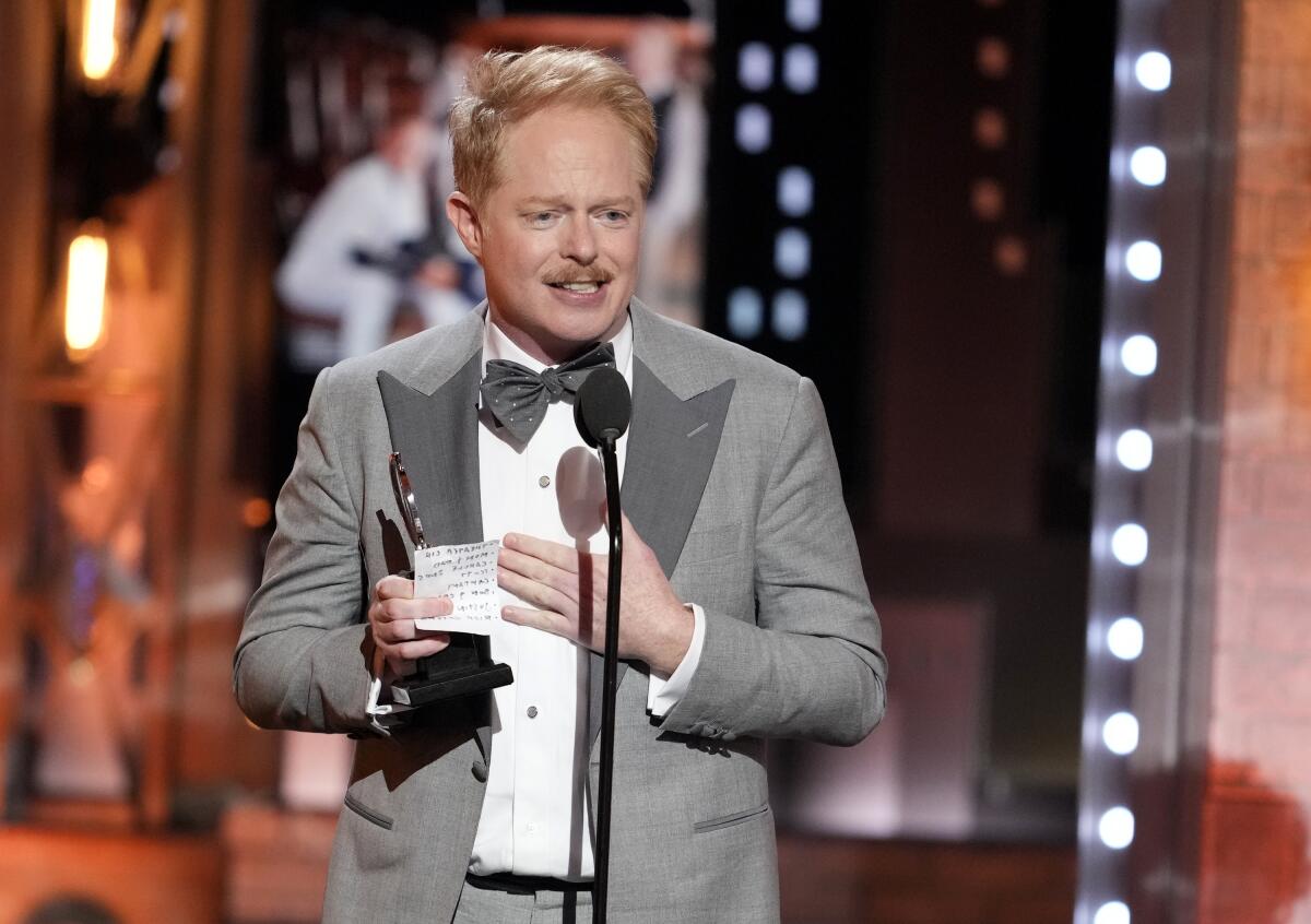 Jesse Tyler Ferguson stands at a microphone holding a Tony Award and a piece of paper.