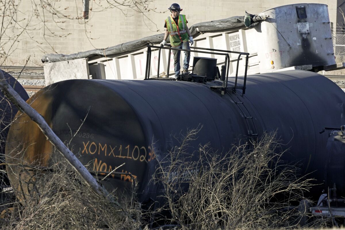 FILE - A cleanup worker stands on a derailed tank car of a Norfolk Southern freight train in East Palestine, Ohio, continues, Feb. 15, 2023. Norfolk Southern is backing away from its push to reduce its train crews down to one person, the company said, Thursday, March 23, 2023, in a joint announcement with the nation’s largest rail union. (AP Photo/Gene J. Puskar, File)