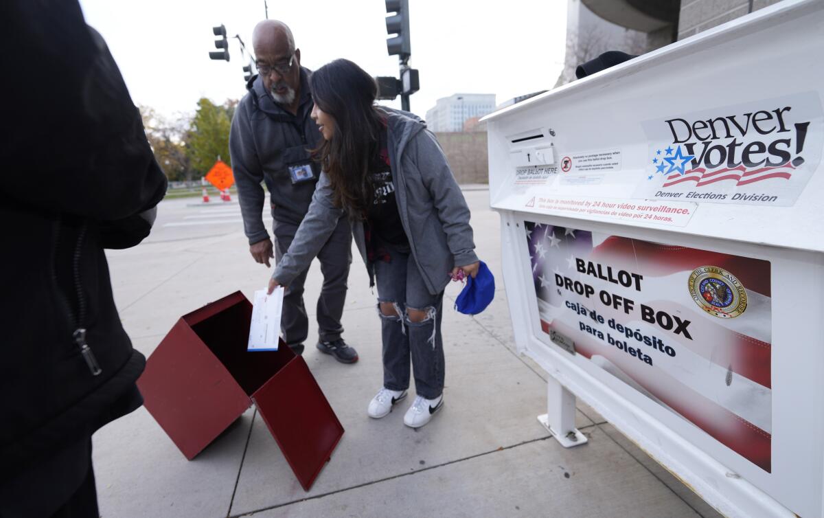 A voter places a ballot into a box next to a labeled Denver ballot drop off spot 