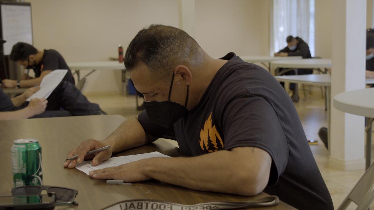 A man sits at a desk with a pen in his hand, leaning over a piece of paper