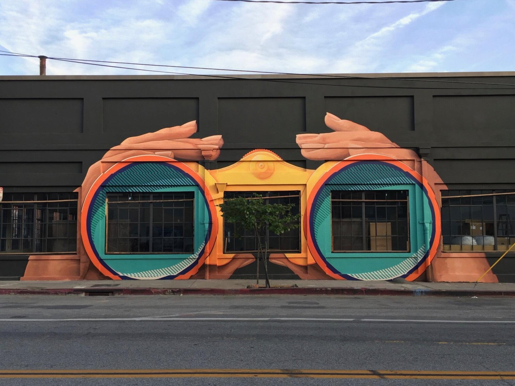 A mural in downtown L.A. depicts hands wrapped around binocular lenses, cleverly painted around the building's windows.