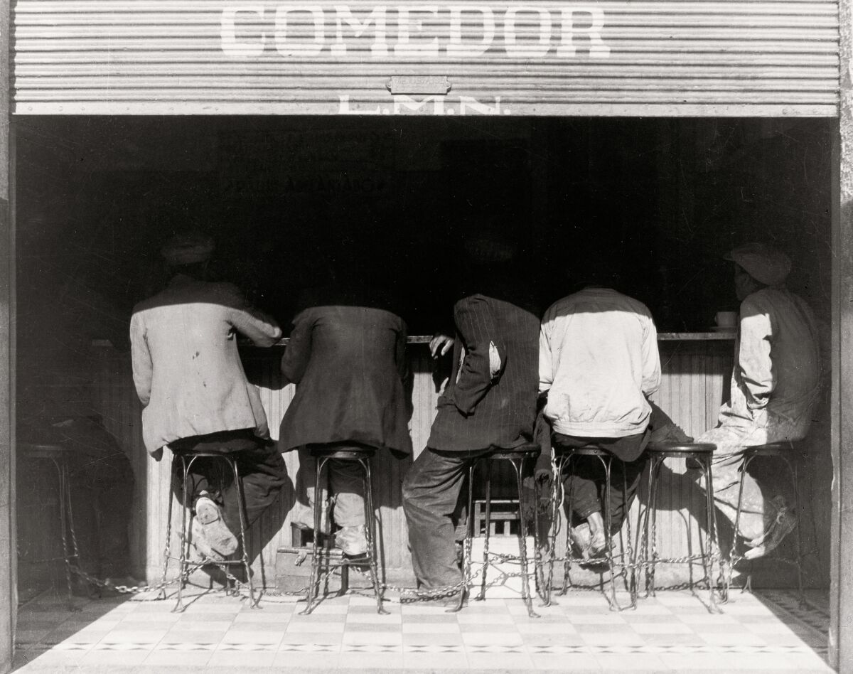 A black-and-white image of people seated on stools at a counter, seen from behind
