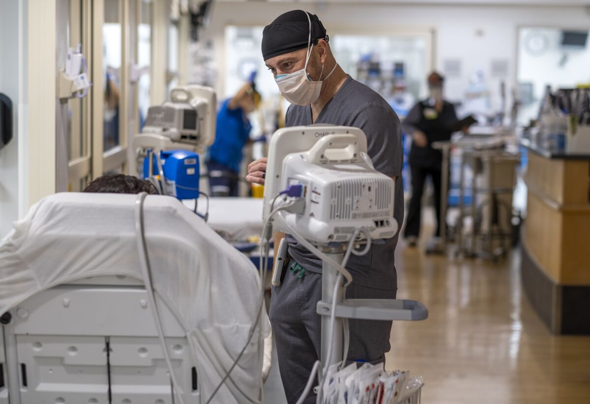 A doctor speaks to a patient in a bed in the hallway of a hospital.