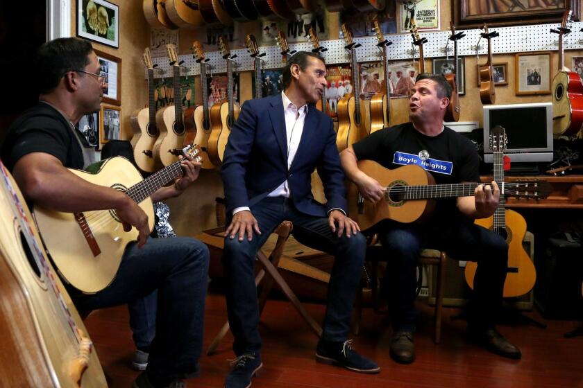 LOS ANGELES, CA- May 25, 2018: Antonio Villaraigosa, center, sings with Tomas Delgado, left, the owner of Candelas Guitars, left, and George Magallanas, right, a friend of Delgado's, as he campaigns in the Boyle Heights neighborhood of Los Angeles, visiting businesses and meeting with small business owners. (Katie Falkenberg / Los Angeles Times)