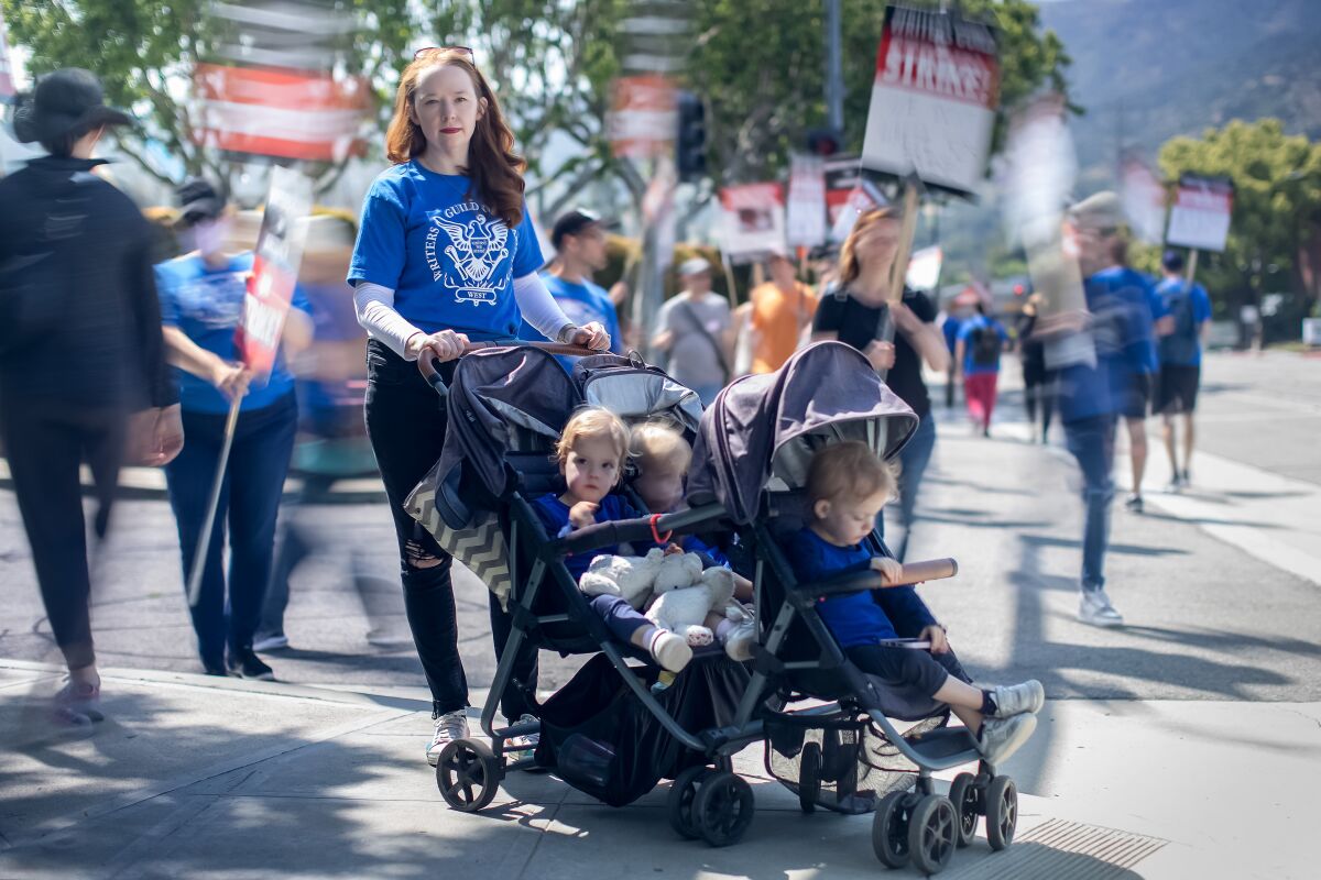 A woman pushing triplets in a stroller pauses from walking a picket line behind her.