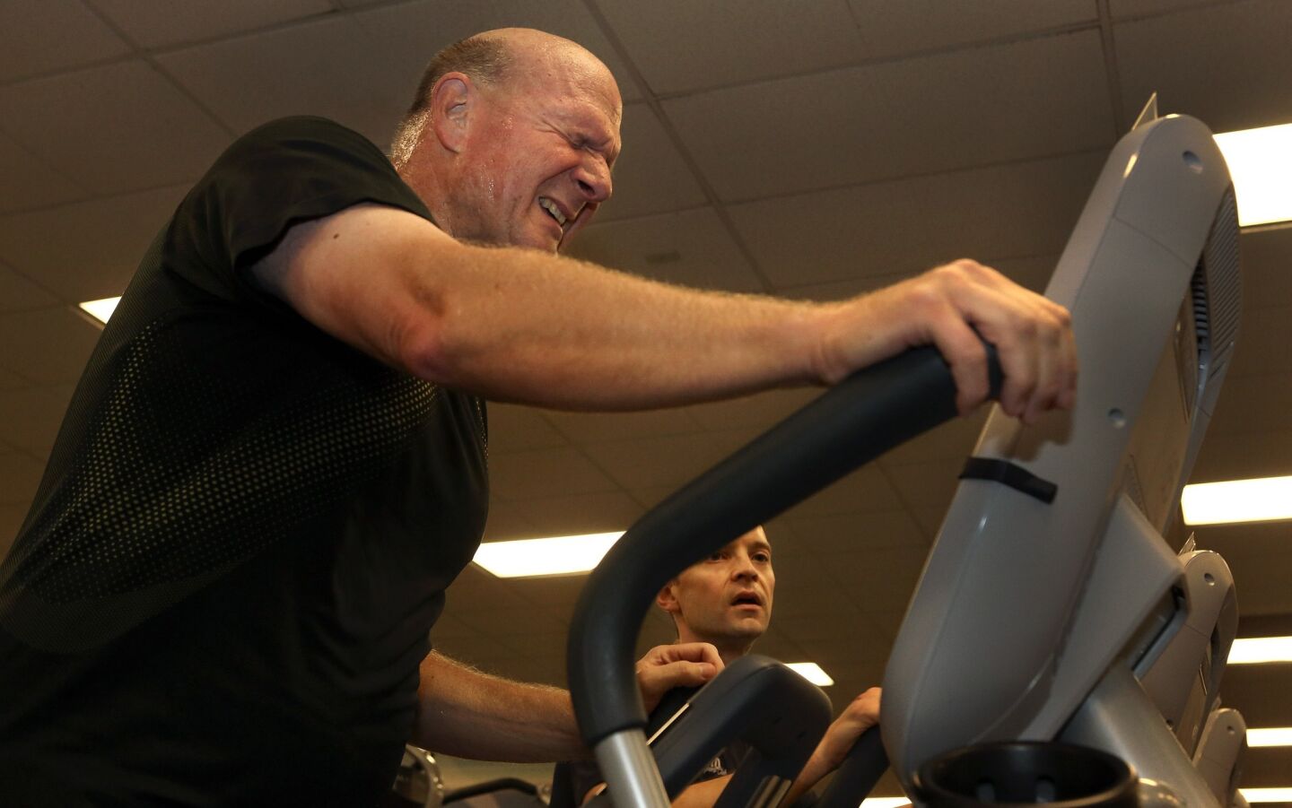 Clippers owner Steve Ballmer grimaces while working out on an elliptical machine at Pro Sports Club in Bellevue, Wash. At right is his trainer Carl Swedberg.