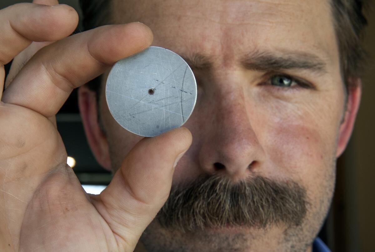 A man holds up a small metal disk with a tiny hole in the center.