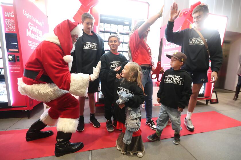 Santa high-fives Rose Stokes, with the rest of the family, Legend, Maze, Tia (mom), Tazz, and Major, from left, after they officially opened the iconic red "Giving Machines" to Southern California with an official launch event, on "Giving Tuesday", at Pacific City in Huntington Beach on Tuesday.