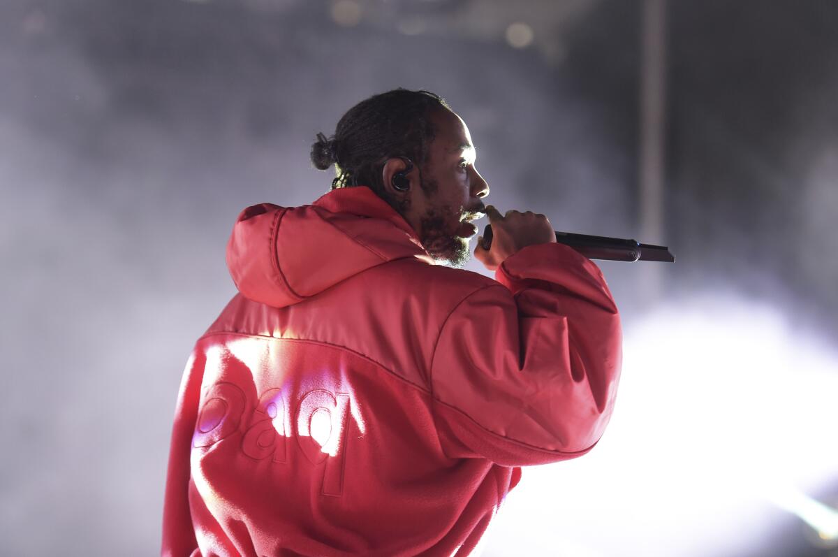 Kendrick Lamar wearing an oversized red jacket and singing into a mic toward the right side of the frame
