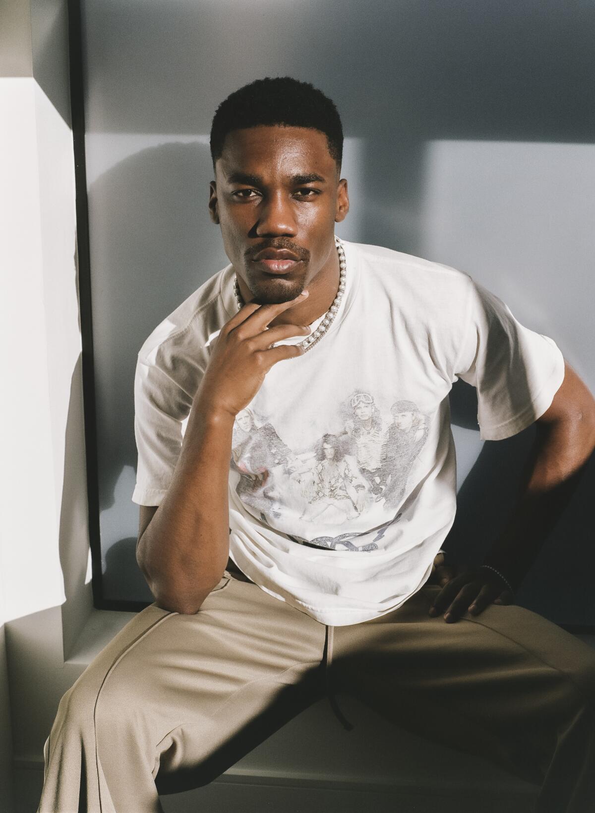 A man, seated, in a white T-shirt and tan slacks