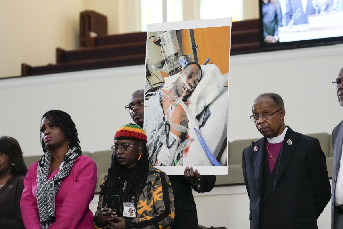 A man, standing with others, holds a photo showing Tyre Nichols in a hospital bed