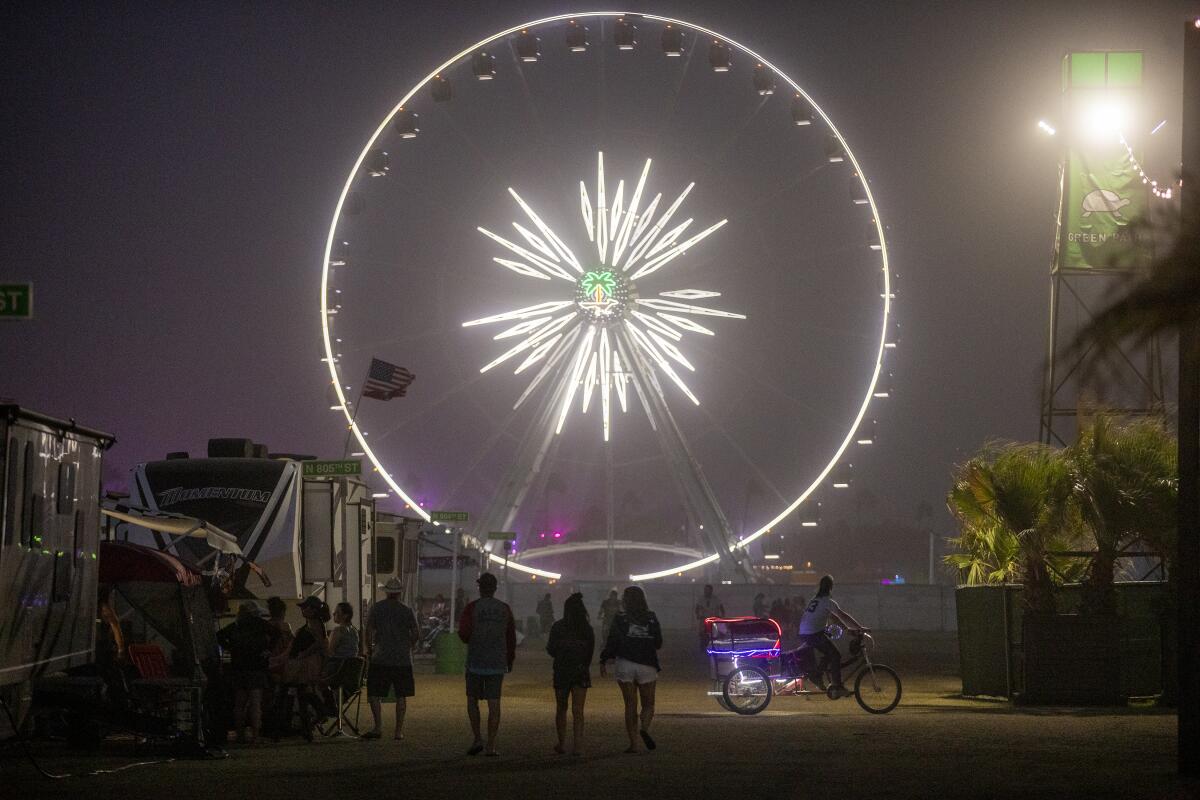 Stagecoach attendees walk at night toward a lighted Ferris wheel on festival grounds