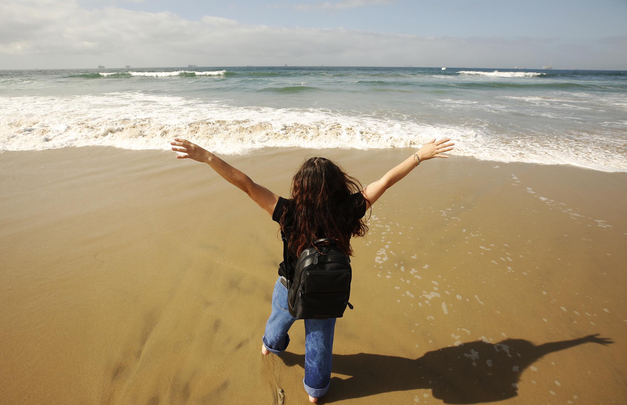 A person at the beach spreads their arms while facing the ocean