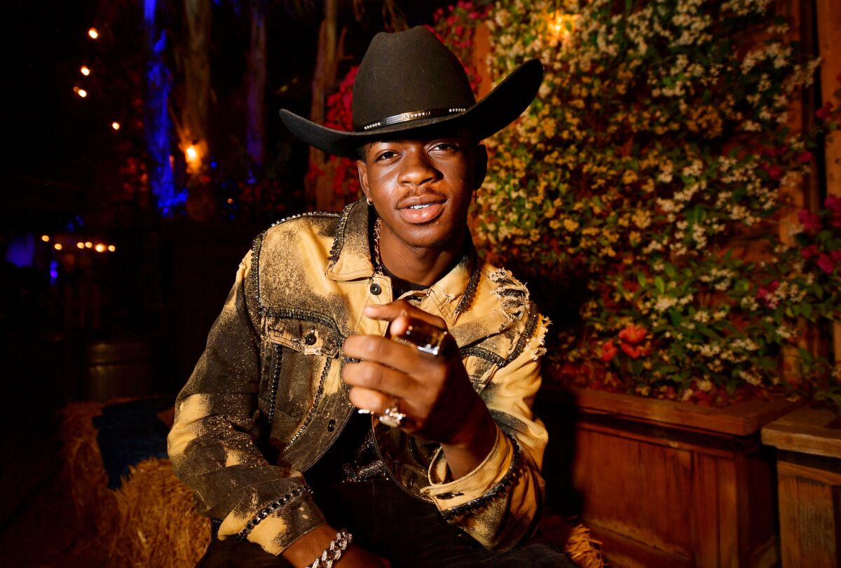 Wearing a cowboy hat, Lil Nas X points at the camera