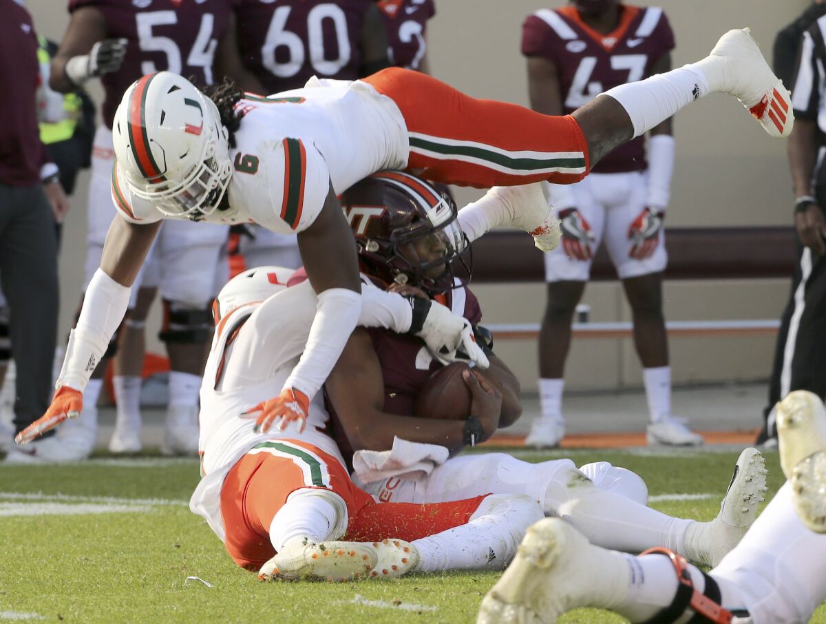 Virginia Tech quarterback Hendon Hooker, center, is tackled by Miami defenders, Sam Brooks, Jr., top, and Jaelan Phillips.