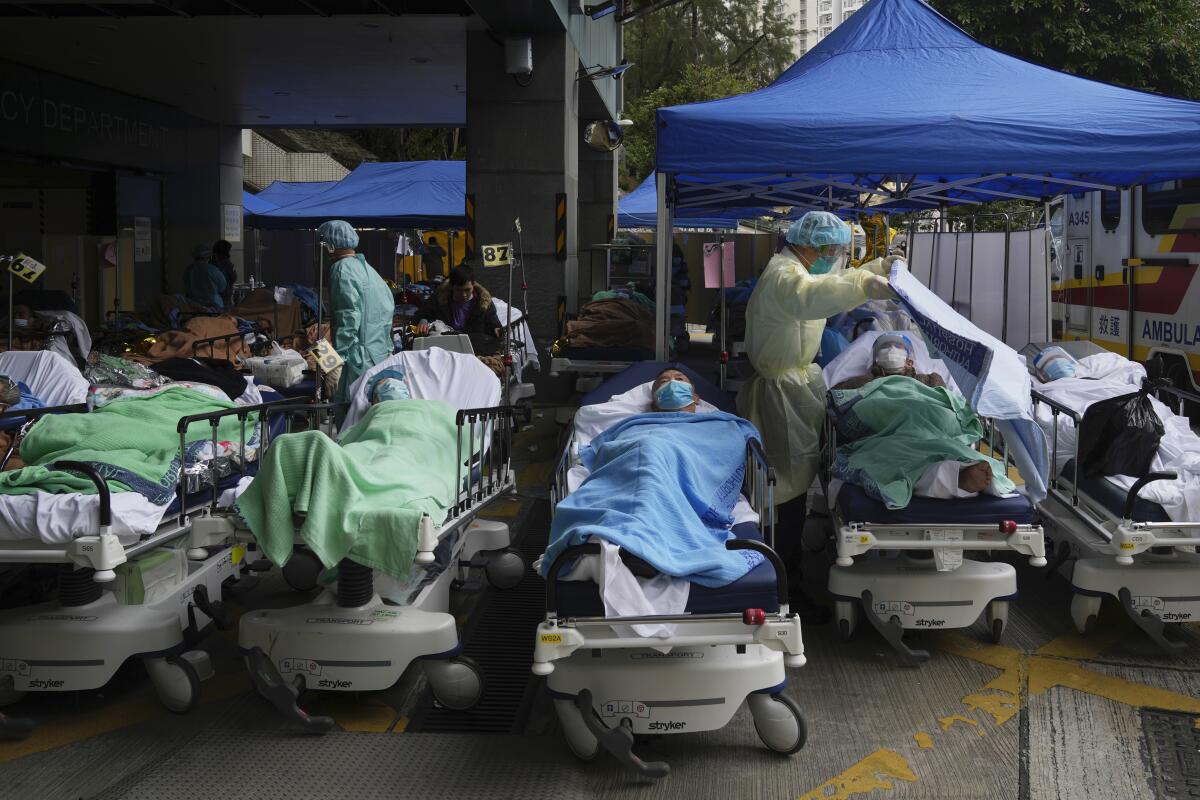 Masked people lie in hospital beds, some under tents, outside a building 
