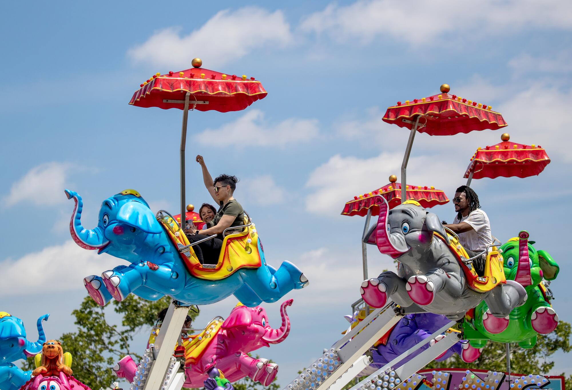 A low angle frame of people riding plastic elephants with umbrellas above them.